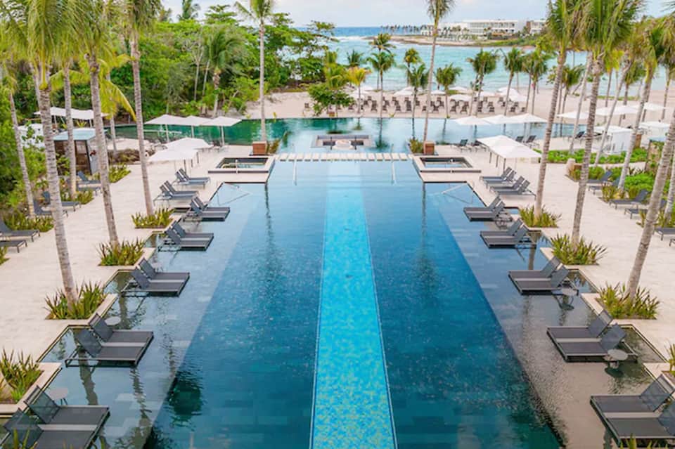 Aerial view of resort infinity pool with palm trees and ocean beach in background