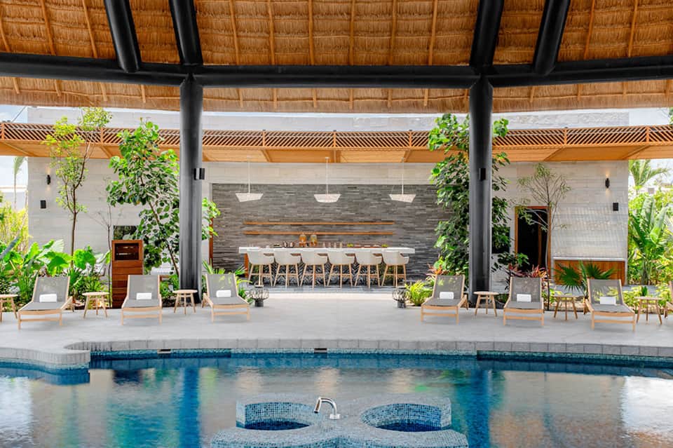 Resort pool pavilion with thatched roof, dining tables, lounge chairs, and tropical landscaping