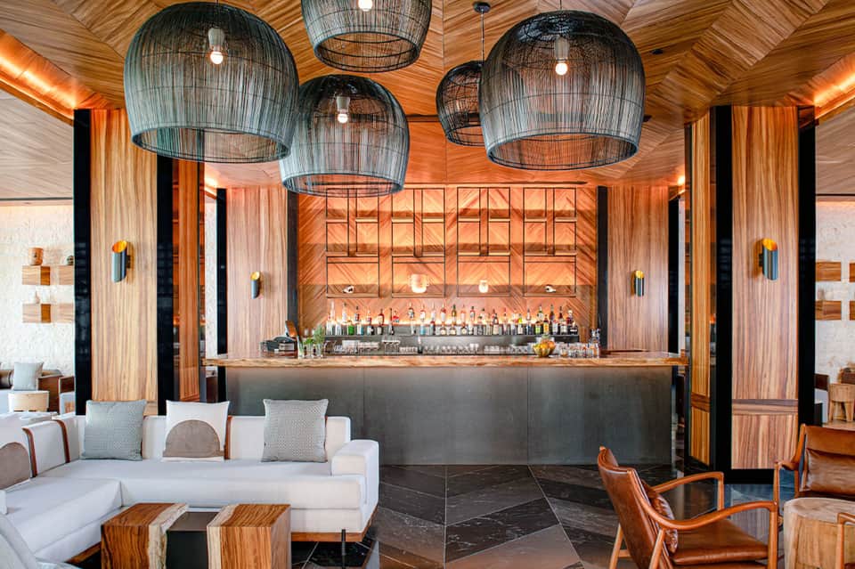 Modern bar lounge with wooden ceiling, woven pendant lights, white sofa, and liquor display