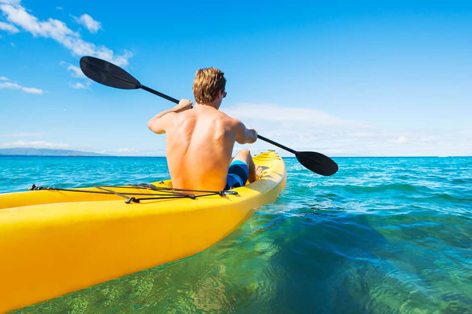Man paddling yellow kayak in clear turquoise ocean water