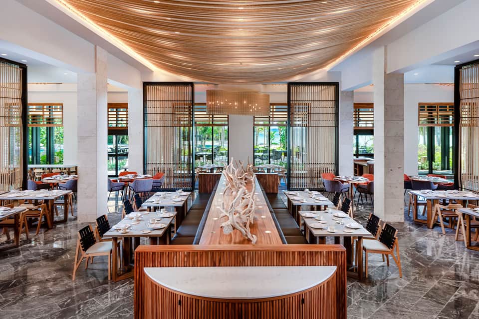 Modern resort restaurant interior with wooden ceiling design, tables, and ocean views through windows
