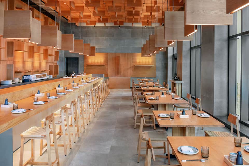 Modern minimalist dining room with natural wood tables, chairs, and copper ceiling panels
