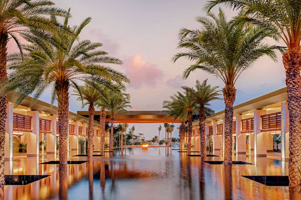 Elegant outdoor corridor with palm trees reflecting in still water at twilight