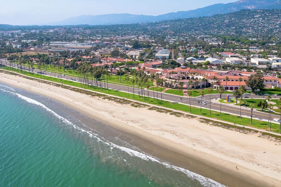 Coastal beachfront area with sand, grass, and residential buildings