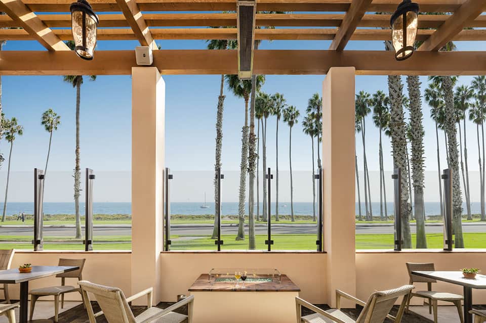 Oceanfront pergola dining area with palm trees, glass railings, and ocean horizon view