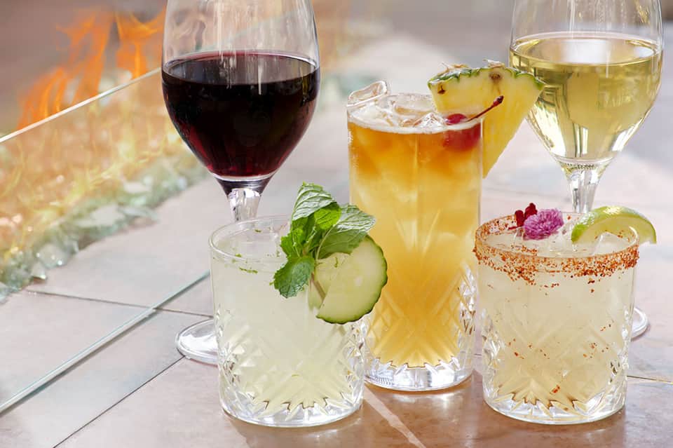 Colorful cocktails with fire, garnishes, and wine served poolside at outdoor bar
