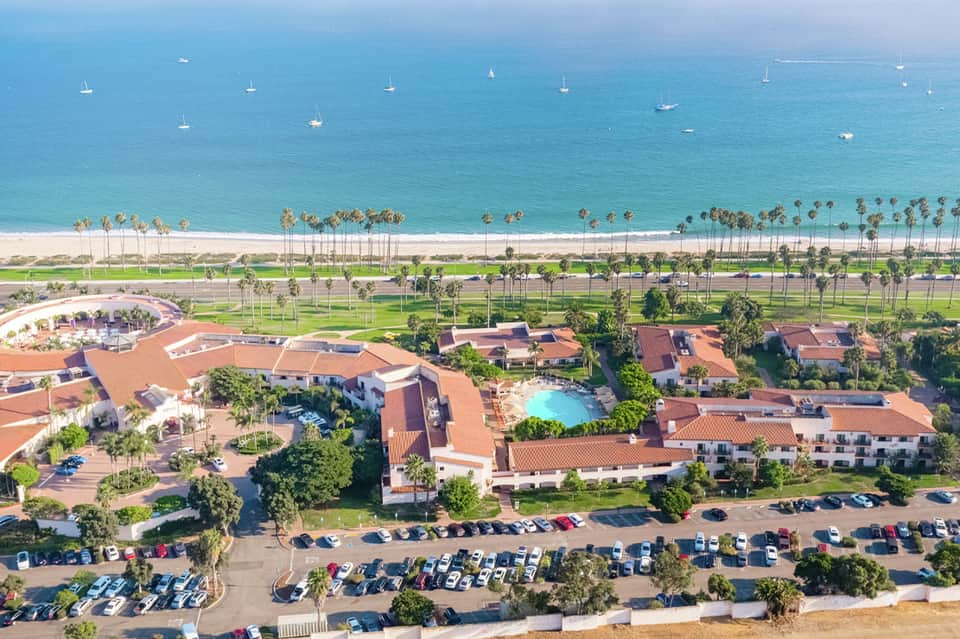 Aerial view of beachfront resort complex with pools, Spanish-tile roofs, palm trees, and ocean view
