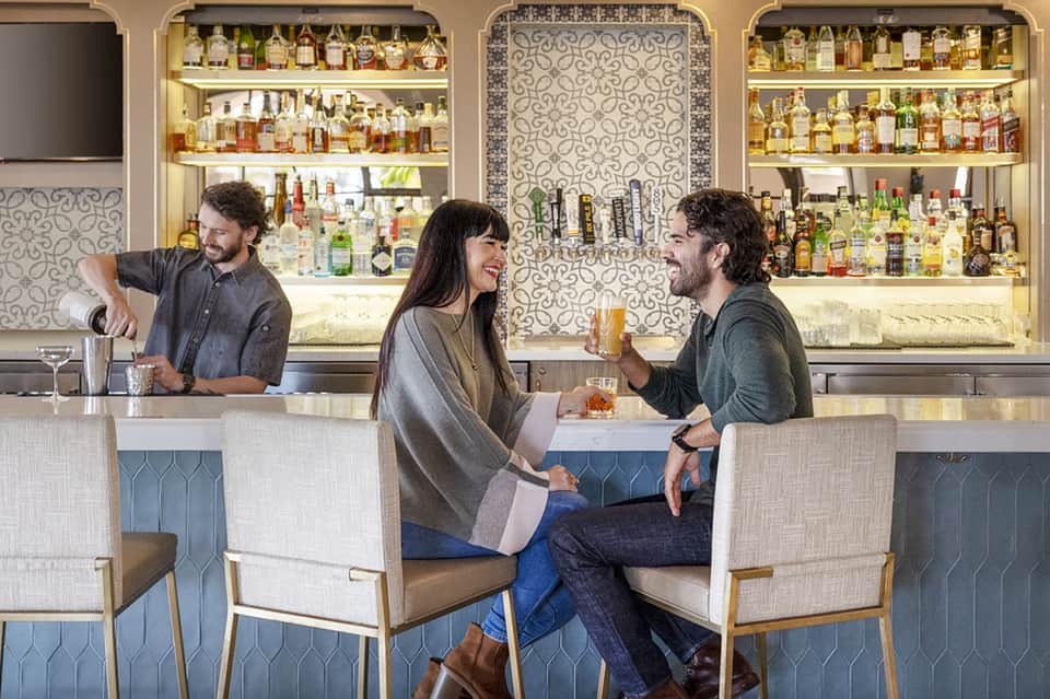 Hotel bar with backlit shelves of liquor bottles and bartender serving customers