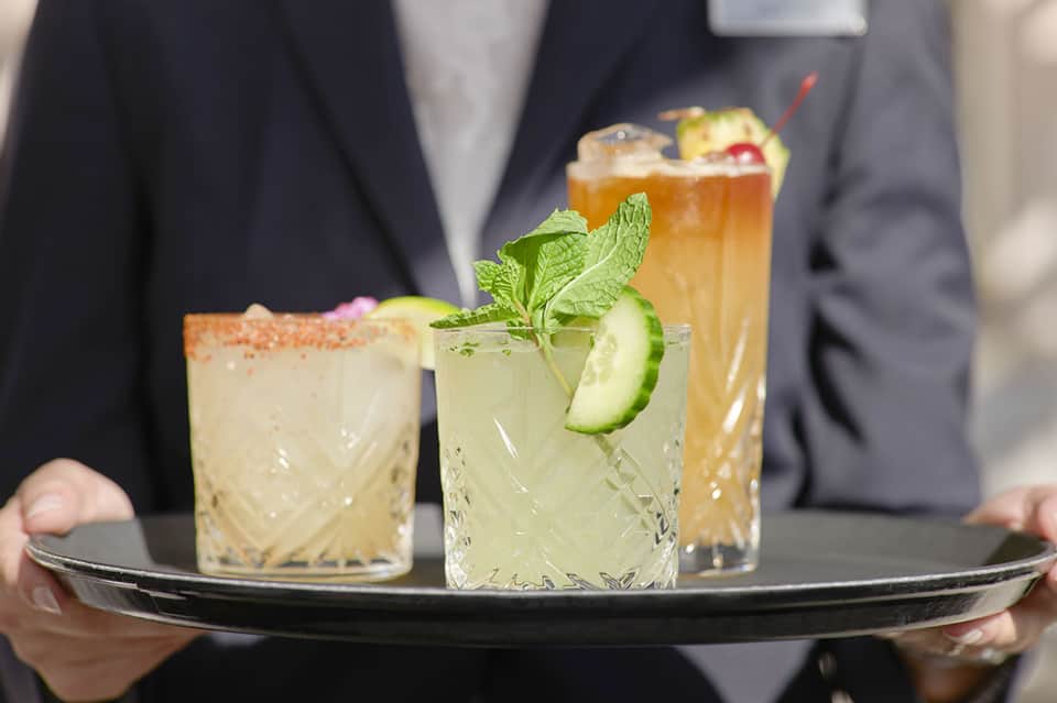 Bartender serving three craft cocktails on a black tray with fresh garnishes and mint