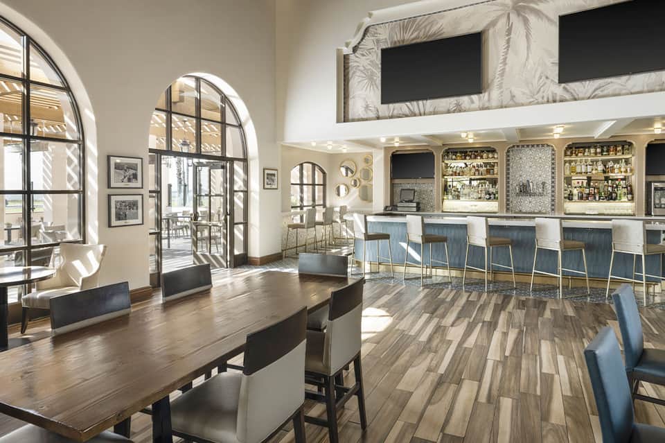 Modern hotel bar and lounge with wooden floors, arched windows, and well-stocked shelves