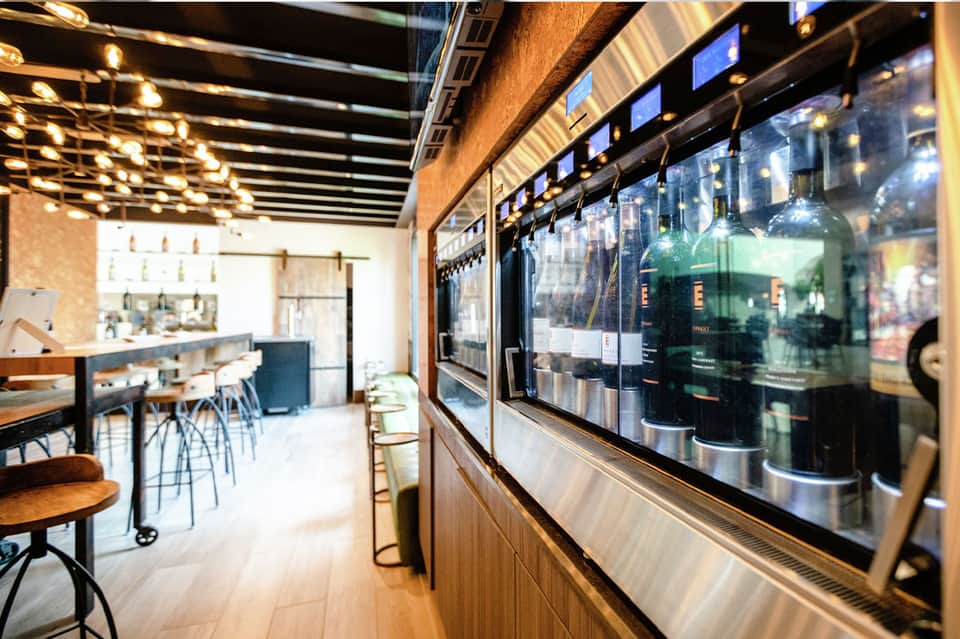 Modern beverage bar with illuminated shelving, glass display cases, and contemporary counter seating