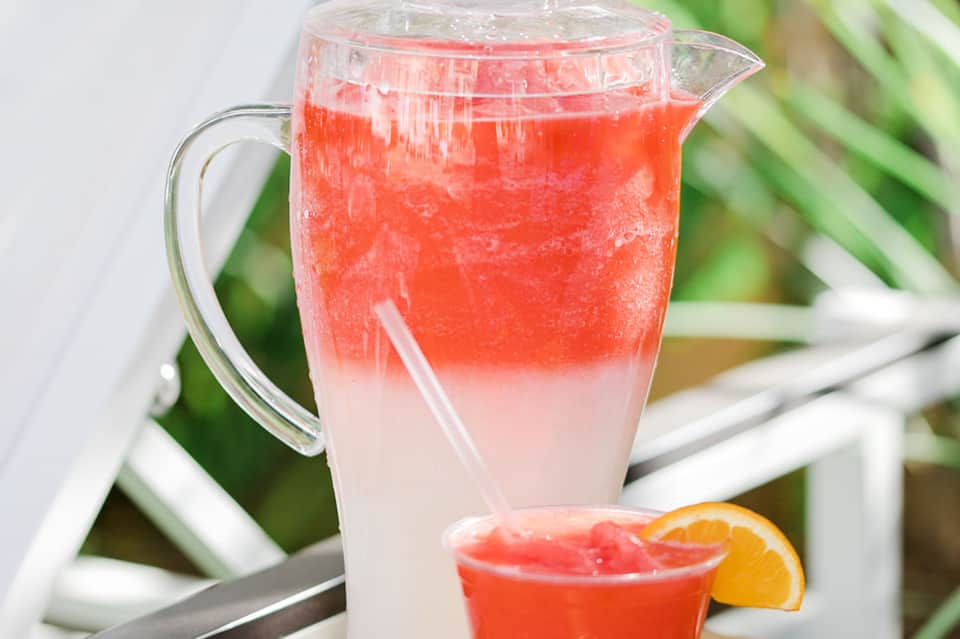Pitcher and glass of refreshing red tropical punch with orange slice garnish