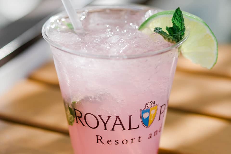 Pink cocktail with lime garnish and mint sprig branded as Royal Resort drink
