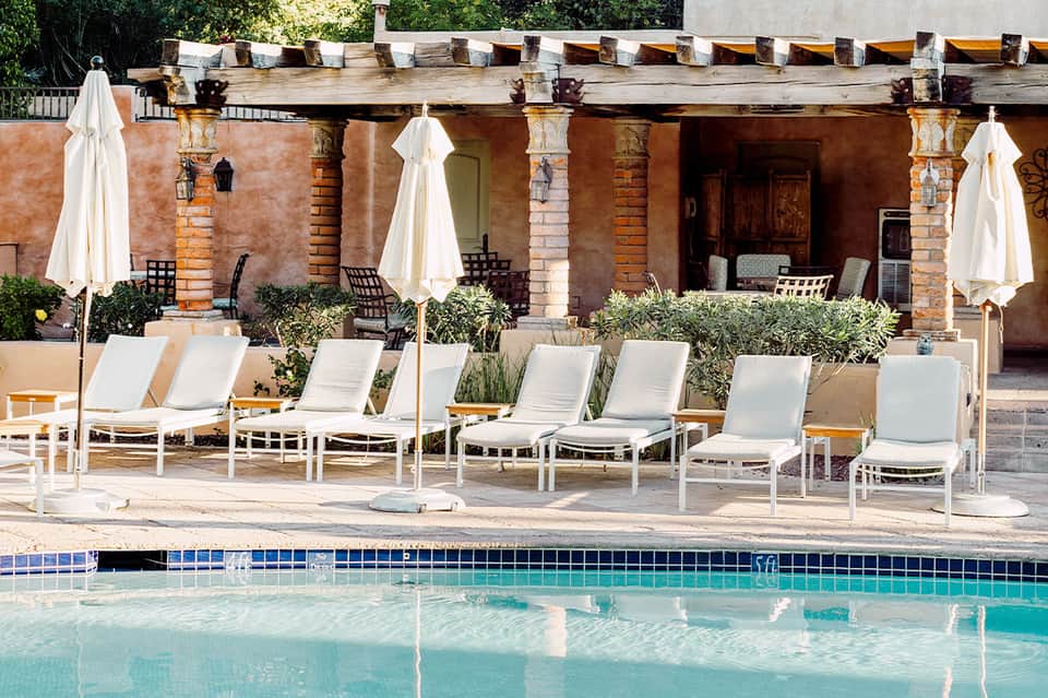 Pool area with lounge chairs, white umbrellas, and rustic brick building with classical columns