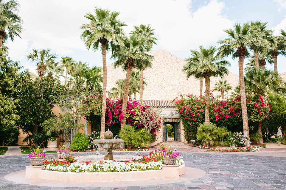 Colonial hacienda courtyard with vibrant pink bougainvillea, palm trees, and fountain