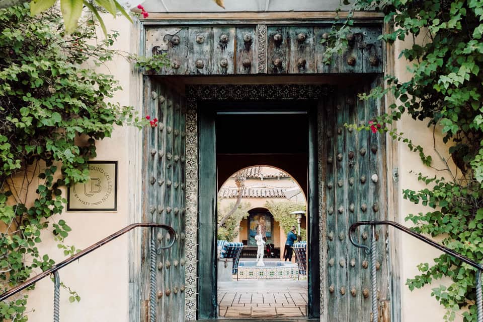 Ornate green doorway framed by ivy leading to courtyard with arches