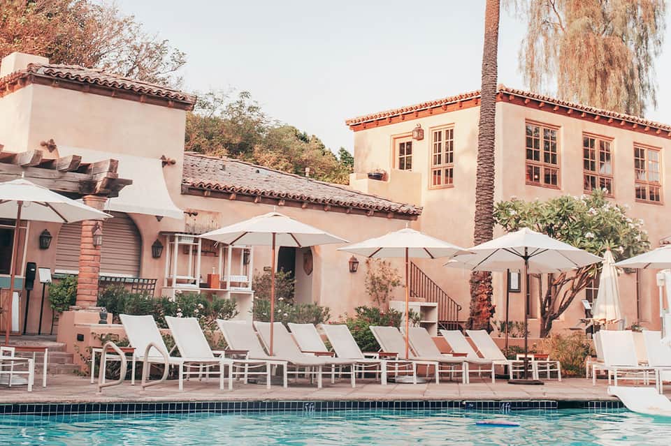 Spanish colonial-style resort courtyard with terracotta buildings, white lounge chairs, umbrellas and pool
