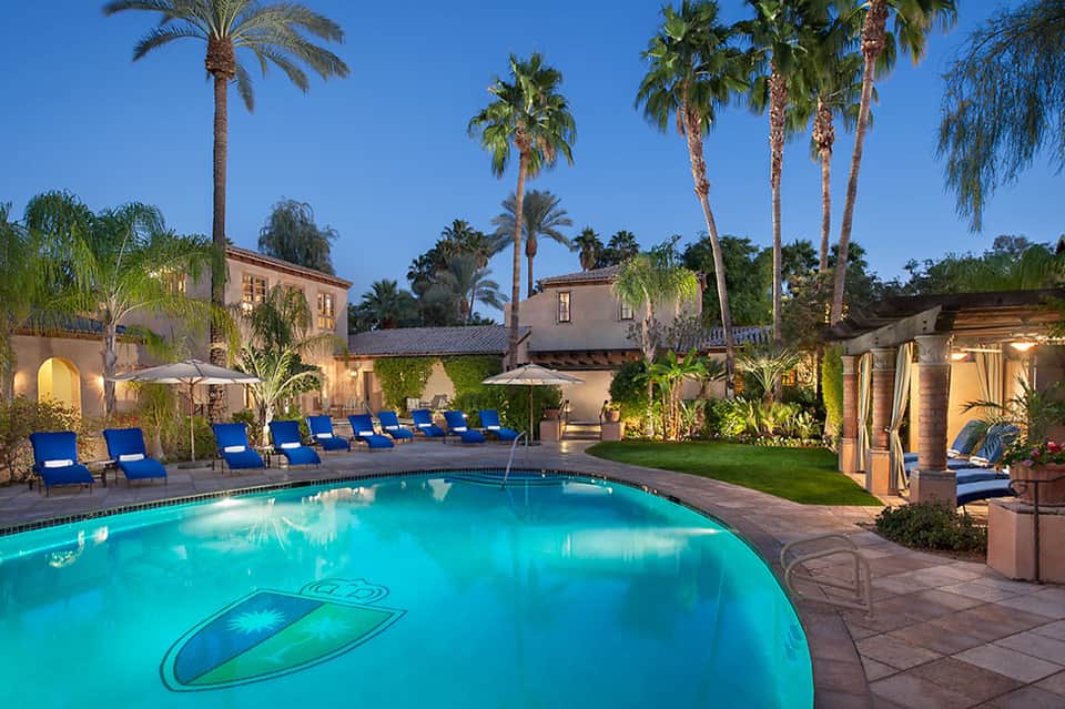 Luxurious resort courtyard with illuminated pool, palm trees, and Spanish colonial architecture at dusk