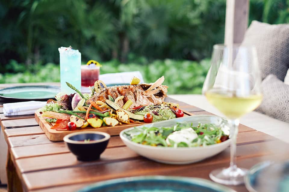 Grilled fish and vegetables on wooden platter with wine and cocktails on poolside table