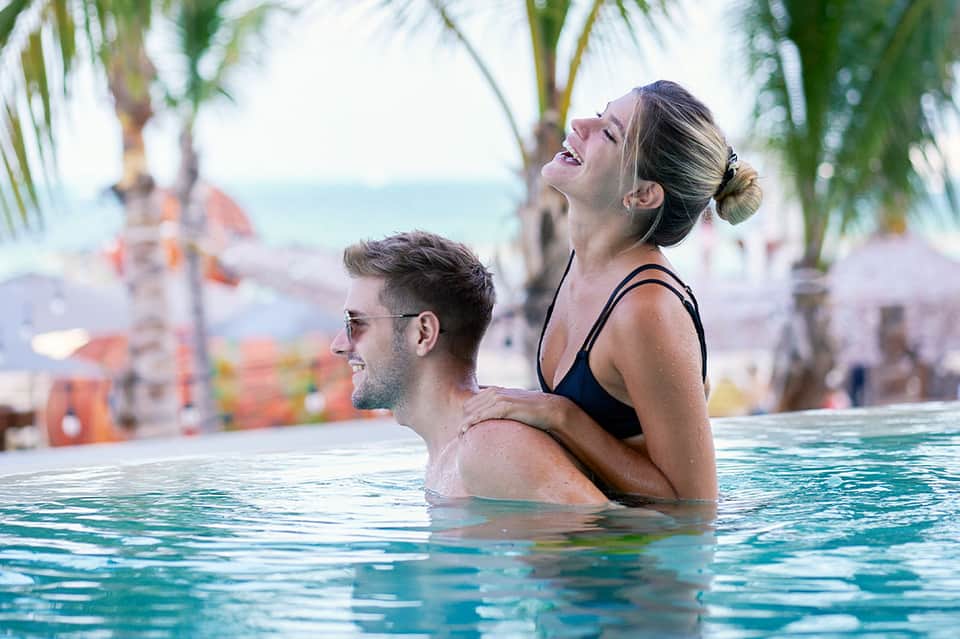Couple relaxing in resort infinity pool with palm trees and ocean view at tropical beach