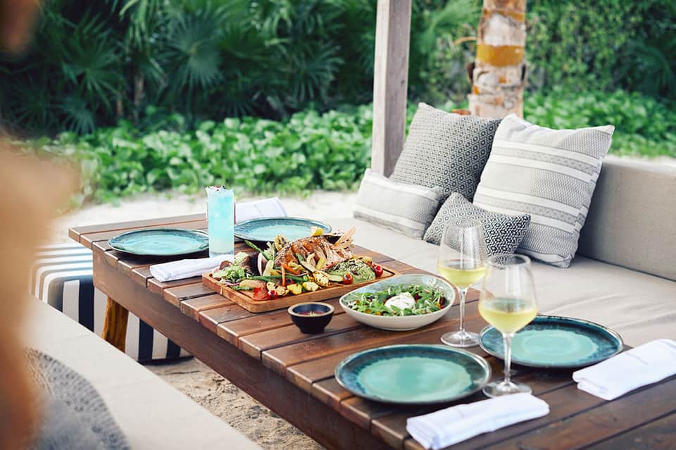 Outdoor dining setup with grilled seafood, salads, and wine glasses on wooden table