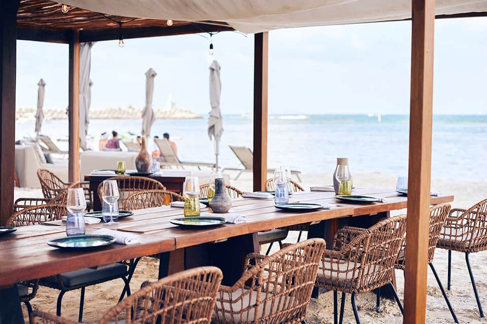 Beachfront dining pavilion with wooden table, wicker chairs, and ocean views