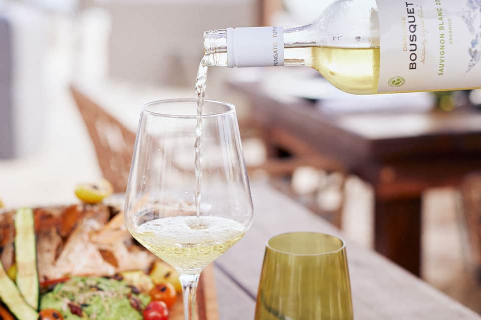 White wine being poured into a glass with Sauvignon Blanc bottle visible