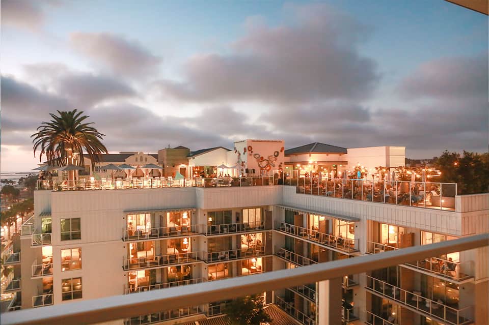 Resort rooftop bar and dining area at dusk with city lights and palm trees