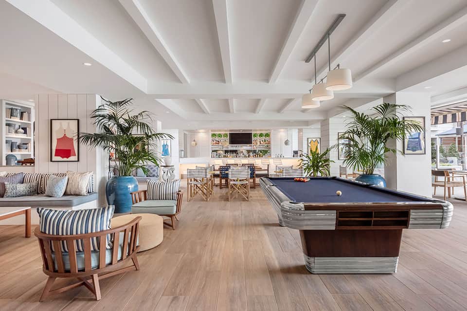 Spacious game room with pool table, bar area, striped seating, and natural light from windows