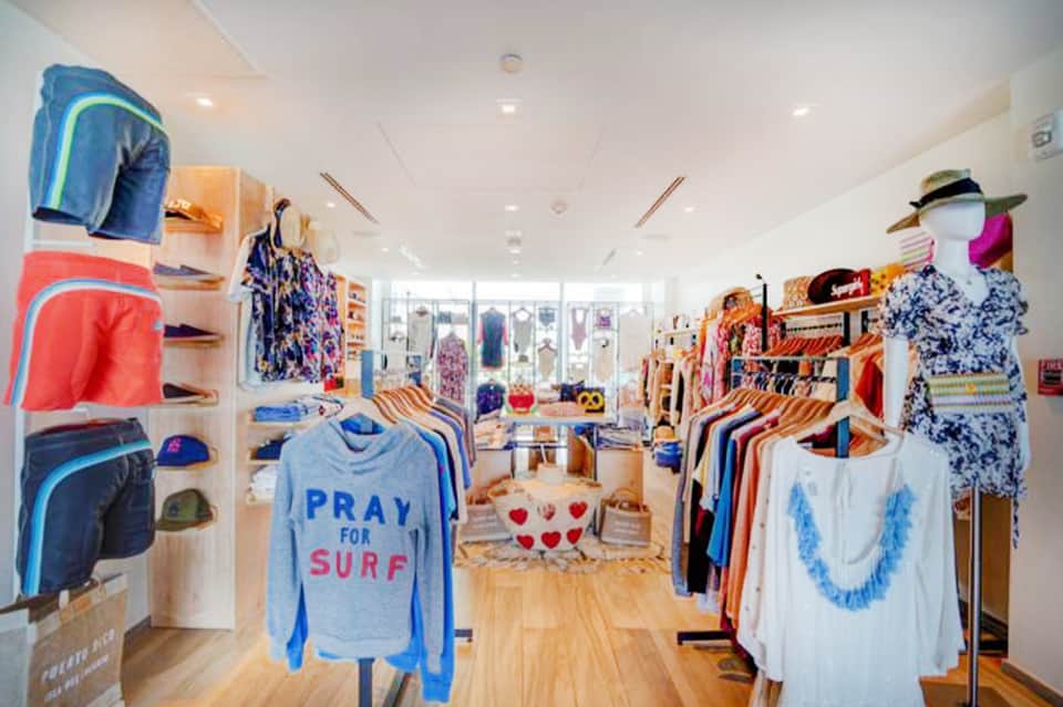 Beachwear retail shop interior with colorful clothing displays, swimwear, and wooden flooring