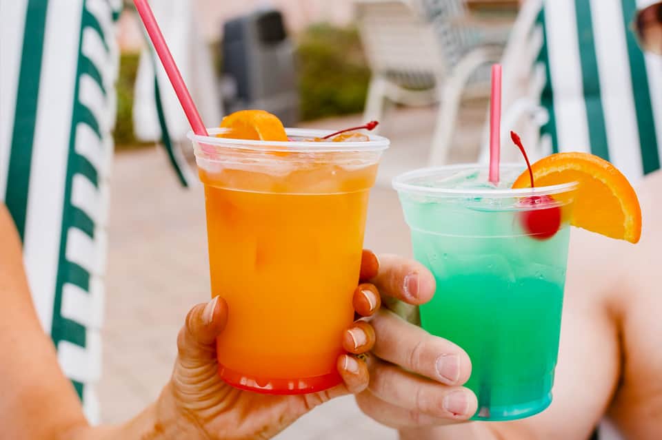 Two colorful tropical cocktails with orange slices and pink straws at a beach resort