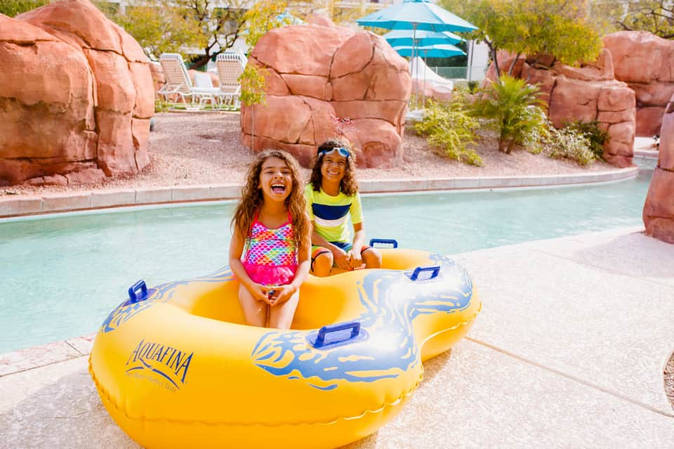 Two young girls in a yellow inflatable boat on a shallow pool surrounded by red rock formations