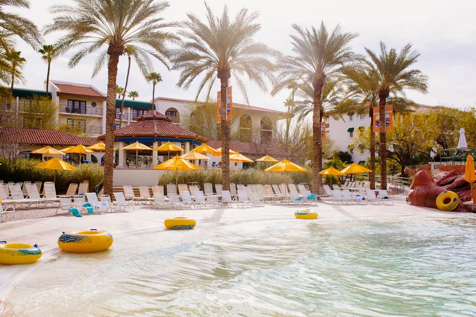 Beach resort with yellow umbrellas, lounge chairs, palm trees, and turquoise water with yellow inflatables