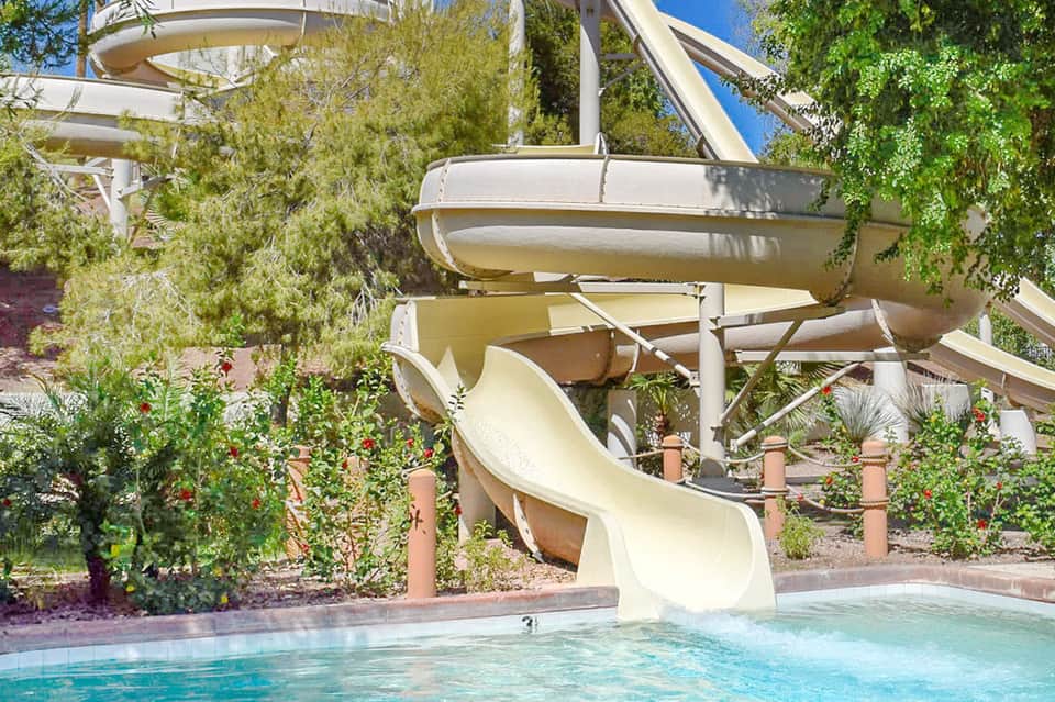 Water slide spiraling into a resort pool surrounded by lush landscaping and palm trees