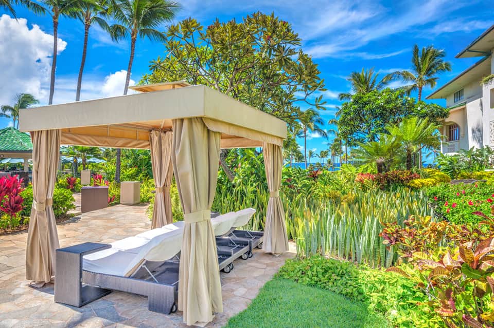 Luxury cabana with cream curtains and loungers in a tropical resort garden with ocean view