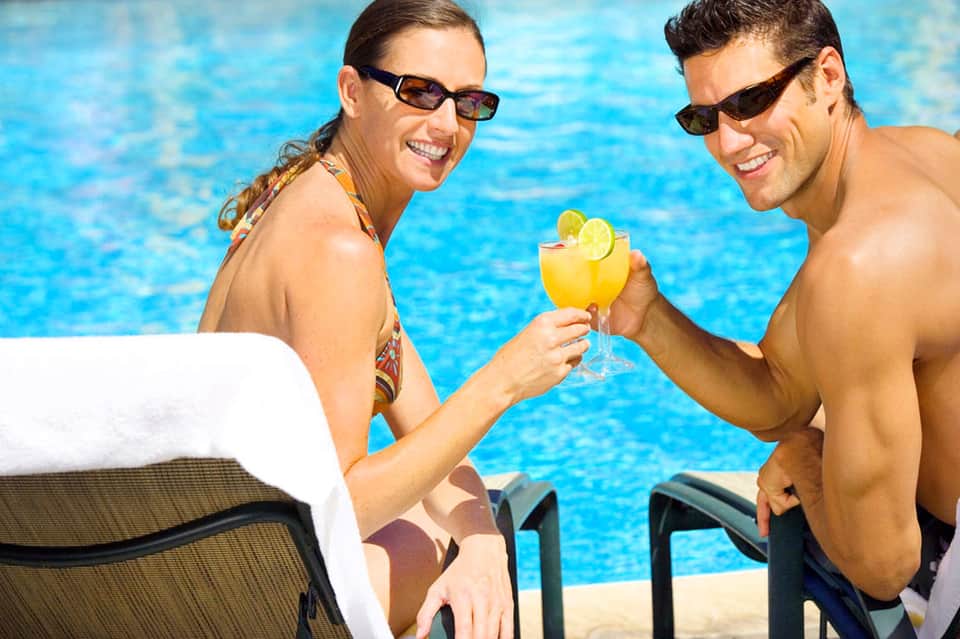Couple enjoying cocktails by outdoor swimming pool in sunny vacation setting