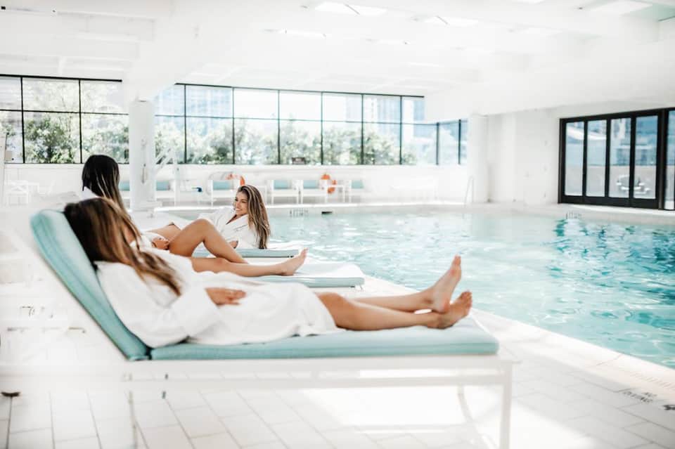 Modern indoor heated pool with lounge chairs, floor-to-ceiling windows, and spa-like ambiance