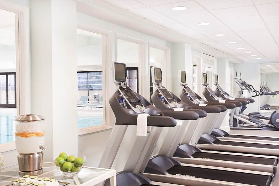 Modern fitness center with treadmills and exercise equipment overlooking indoor pool area