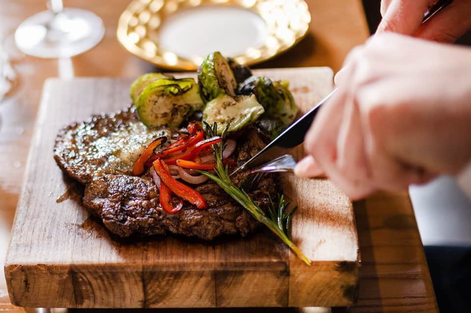 Plated steak with roasted vegetables and herbs on wooden serving board in upscale dining setting
