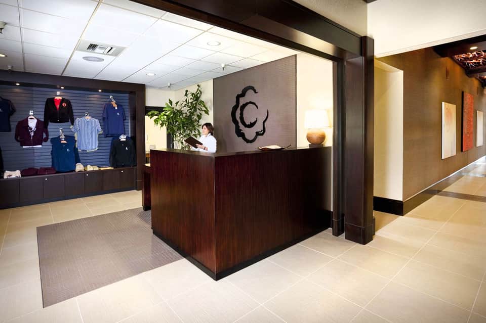 Hotel lobby with dark wood reception desk, clothing displays, and modern décor with plant arrangements