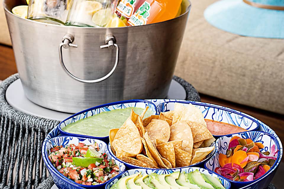 Appetizer platter with chips, salsa, guacamole, and tropical drinks in ice bucket