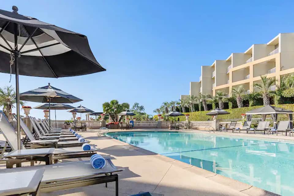 Resort pool with black umbrellas, loungers, and multi-story building with palm landscaping