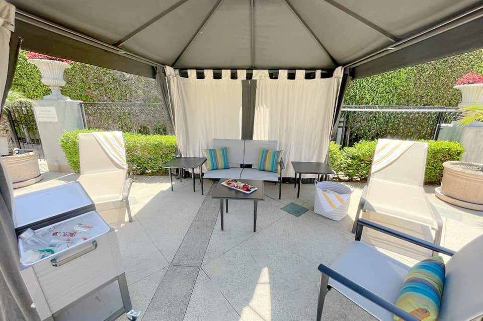 Covered outdoor patio with lounge chairs, cushions, and manicured hedges