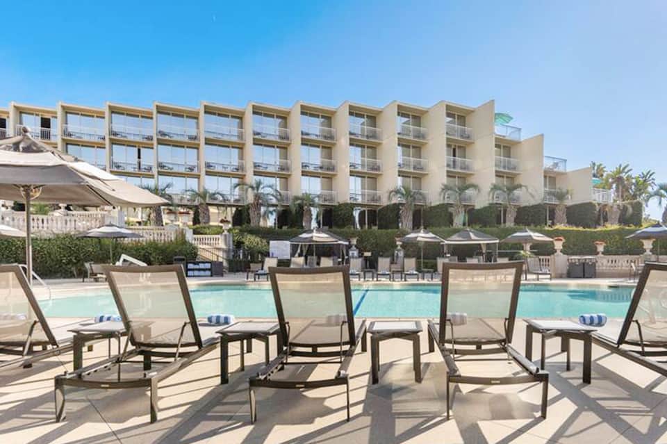Resort beachfront with lounge chairs facing ocean, palm trees, and multi-story hotel building