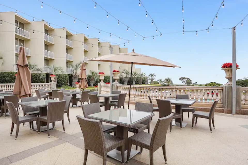 Resort rooftop dining area with tables, umbrellas, string lights, and apartment building backdrop