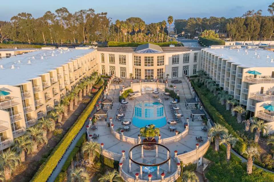 Aerial view of resort with multiple pools, courtyard, surrounding residential buildings and waterfront landscape