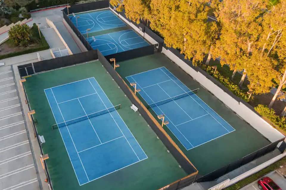 Aerial view of four tennis courts with blue and green surfaces surrounded by autumn foliage