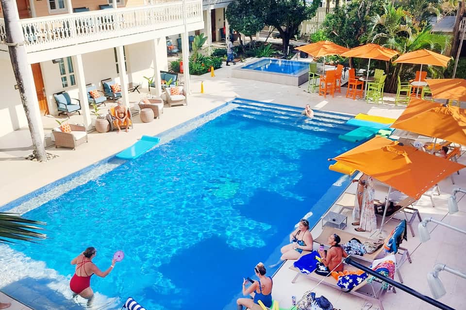 Resort pool with families swimming, orange umbrellas, white building, and lush landscaping
