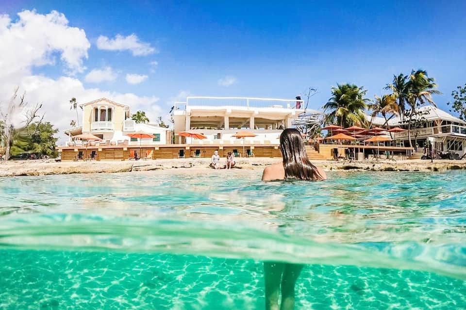 Woman swimming in turquoise ocean water near beachfront resort with palm trees