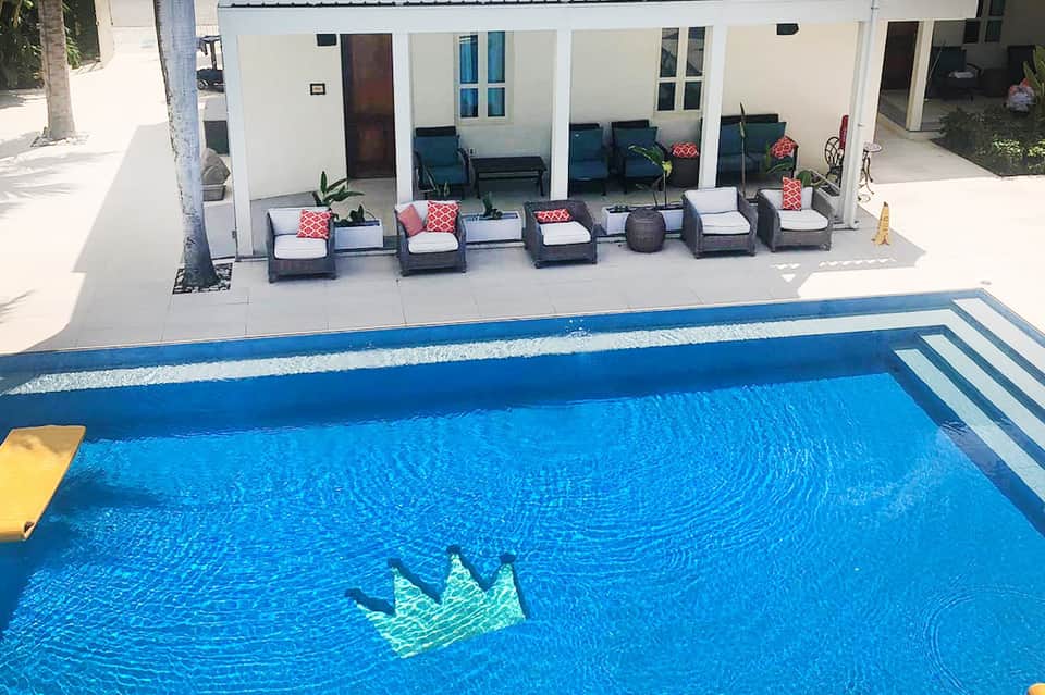 Resort pool with blue water next to white building and padded lounge chairs